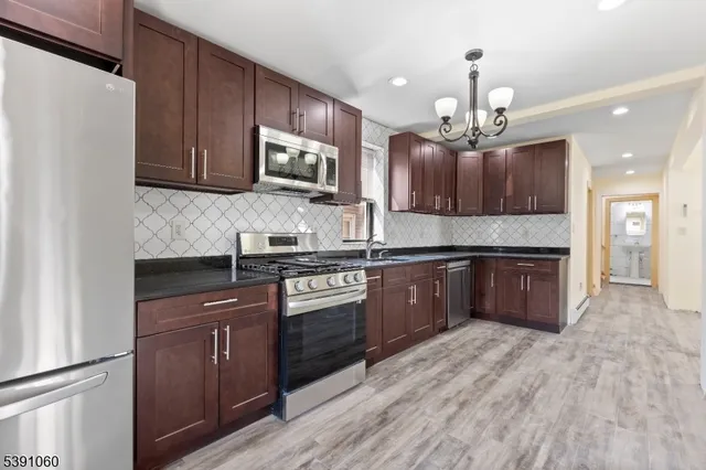 a large kitchen with stainless steel appliances granite countertop a stove a sink dishwasher a refrigerator and a microwave oven with wooden floor