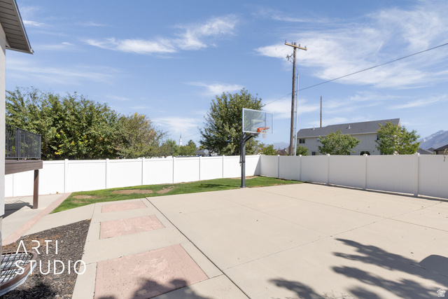 704 West Vahe Street Draper, UT 84020 - Photo 35 of 35 Expansive concrete pad, ideal for recreation, featuring a basketball hoop, surrounded by a white privacy fence
