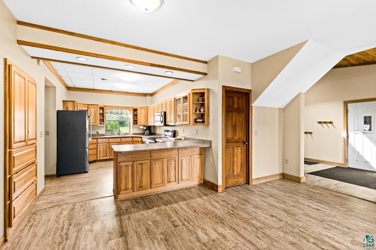 4800 Tower Road Moose Lake, MN 55767 - Photo 9 of 83 Open-concept kitchen featuring wood-finish cabinetry, a large kitchen island with counter seating, and a full suite of black and stainless steel appliances