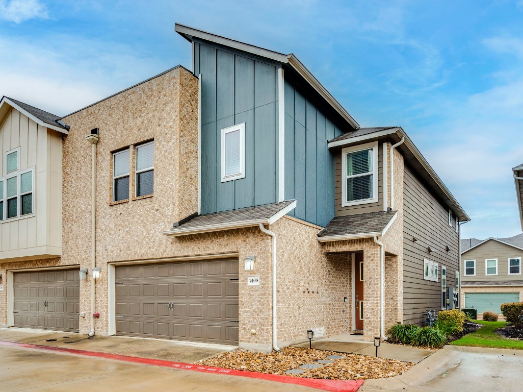 7408 Merrick Lane, Unit 42 Austin, TX 78745 - Photo 2 of 28 View of front of house featuring board and batten siding, an attached garage, driveway, and brick siding and visitor park adjacent
