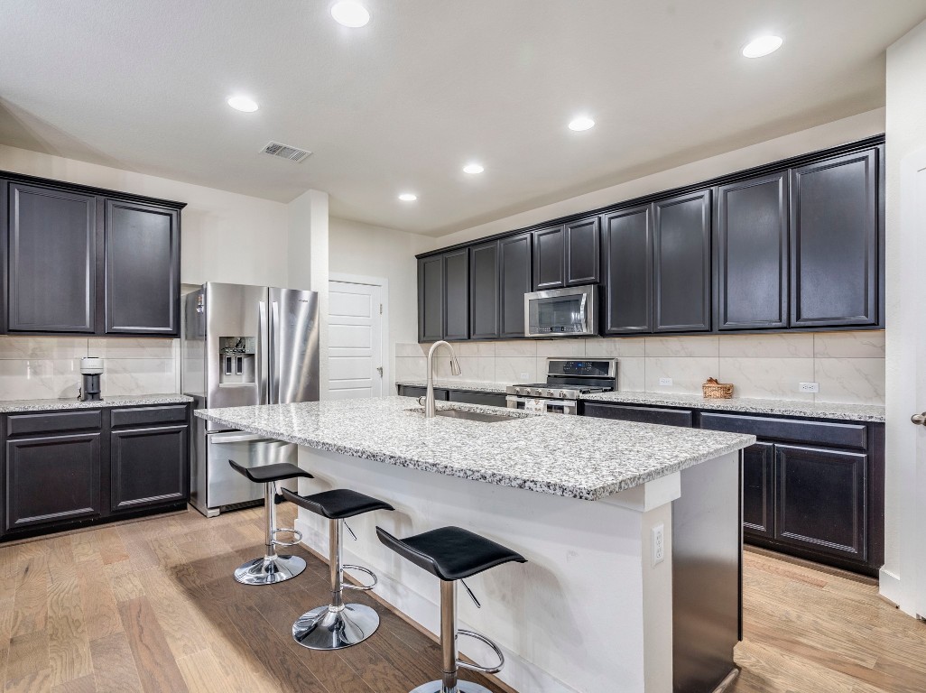 7408 Merrick Lane, Unit 42 Austin, TX 78745 - Photo 6 of 28 Kitchen with tasteful backsplash, appliances with stainless steel finishes, light stone countertops, a kitchen bar, and light wood-style flooring