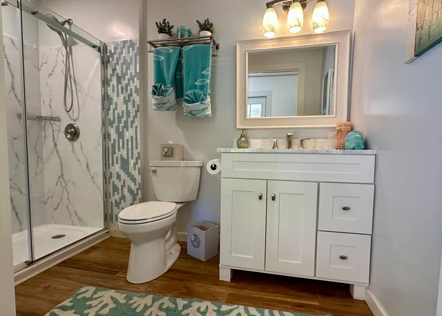 a bathroom with a toilet a sink a glass door a shower a mirror a vanity and window