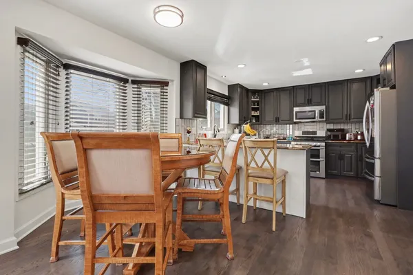 a dining room with stainless steel appliances a dining table chairs and a wooden floor