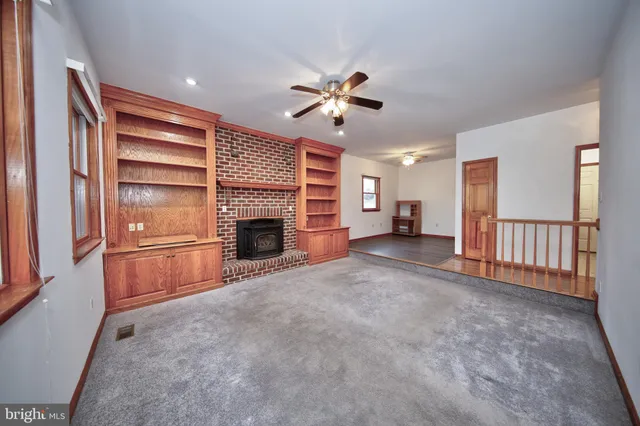 a view of a livingroom with a fireplace a ceiling fan and windows