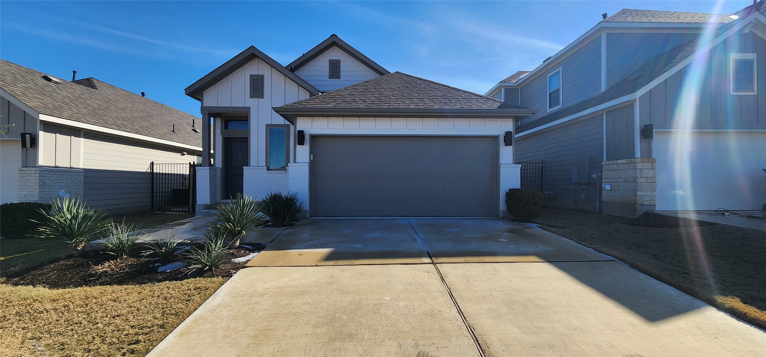 View of front of home with board and batten siding, driveway, an attached garage, and a gate