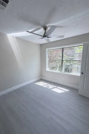 an empty room with wooden floor chandelier fan and windows