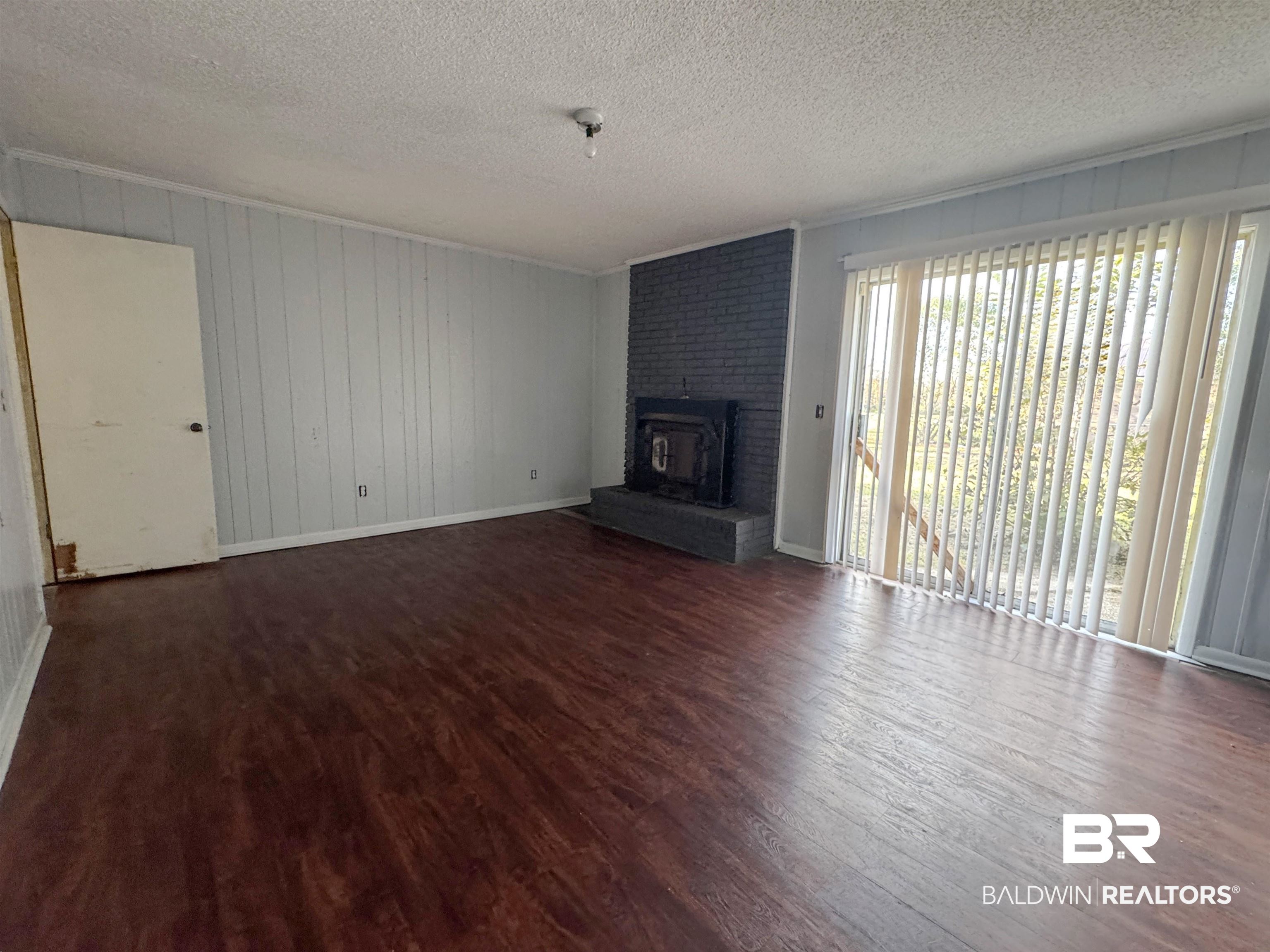 1227 Northgate Drive Atmore, AL 36502 - Photo 6 of 14 Unfurnished living room with dark wood finished floors, a fireplace, a textured ceiling, and wooden walls
