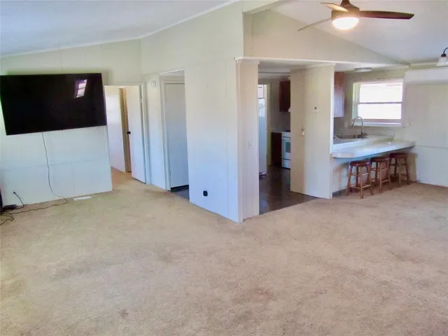 a view of an empty room with wooden floor and a kitchen
