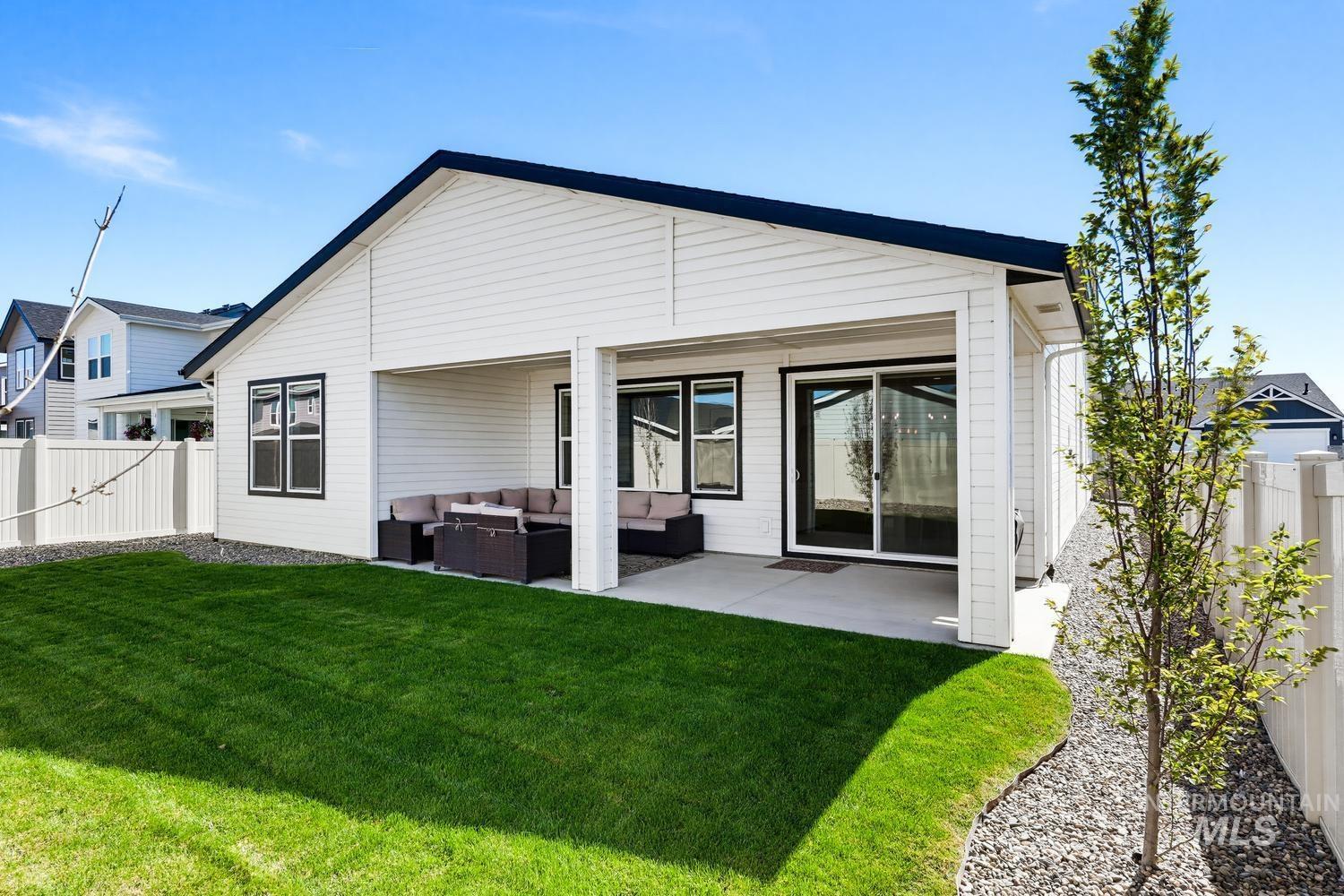 5990 West Ladle Rpds Street Meridian, ID 83646 - Photo 40 of 42 White siding exterior with black trim windows, a covered concrete patio, a sliding glass door, a privacy fence, and a landscaped yard