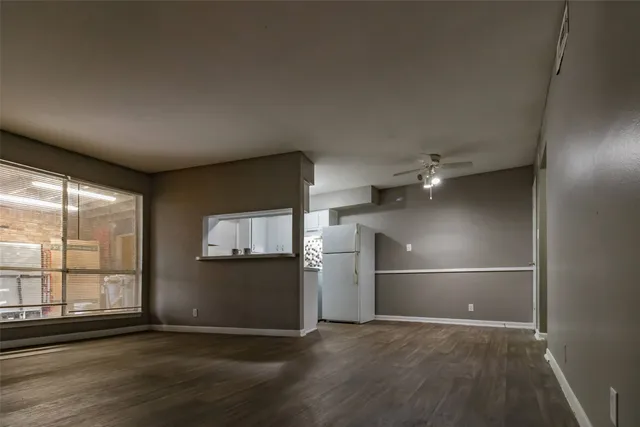 an empty room with wooden floor kitchen view and windows