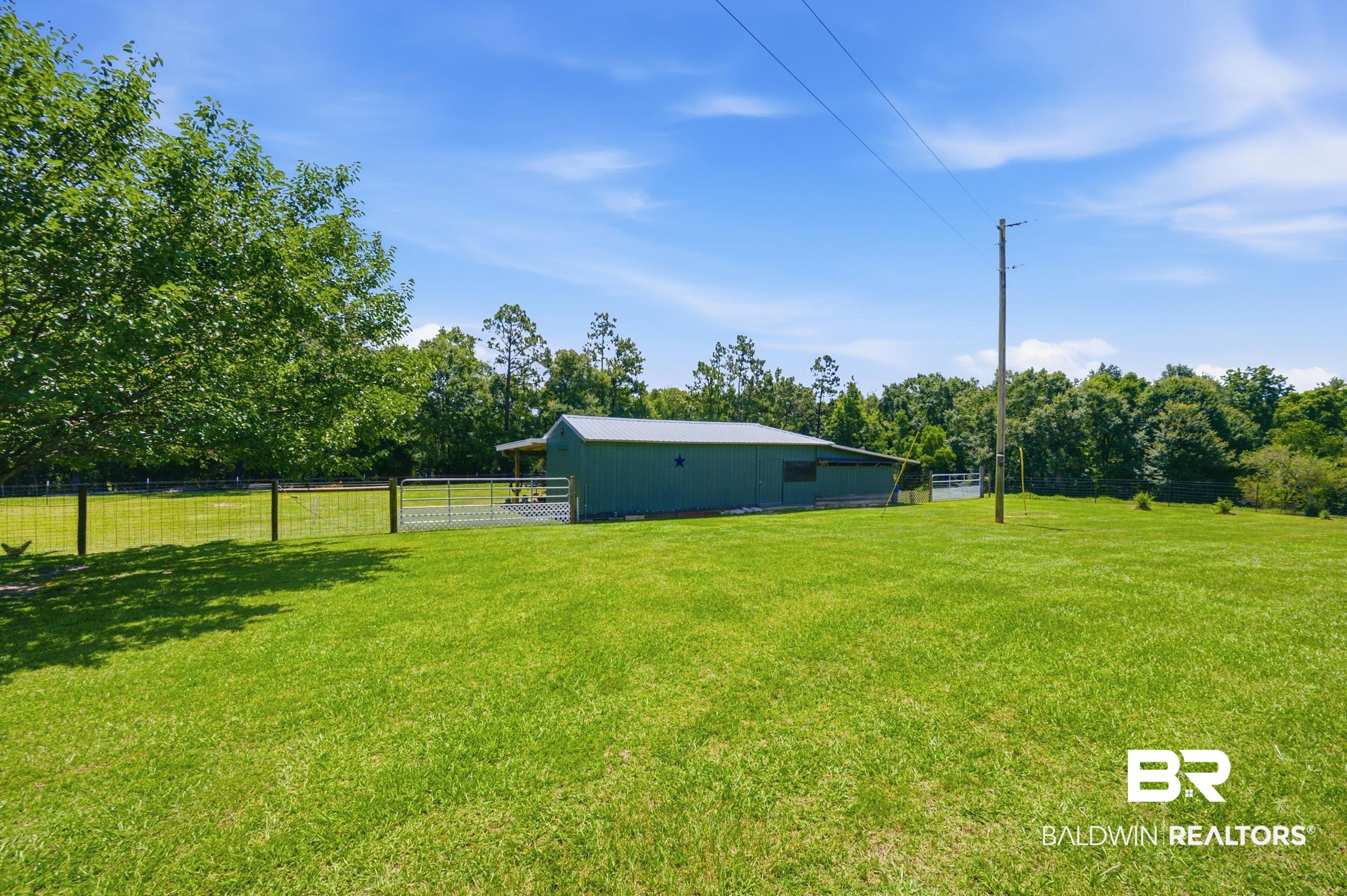 15855 Calvin Richerson Road Bay Minette, AL 36507 - Photo 69 of 83 Expansive green lawn with a metal barn featuring a covered lean-to, perimeter fencing, and mature trees