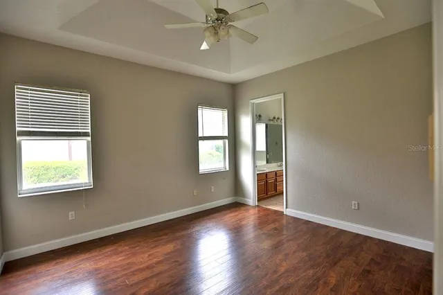 an empty room with wooden floor windows and ceiling fan