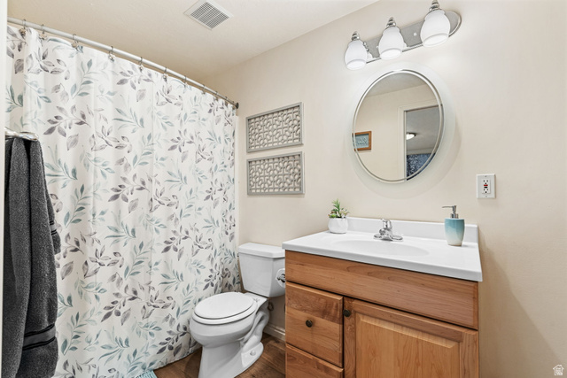 14883 Tooele Lane Draper, UT 84020 - Photo 39 of 49 Bathroom featuring wood-finish flooring, a wood vanity with a white countertop and integrated sink, a circular mirror, and a three-light fixture