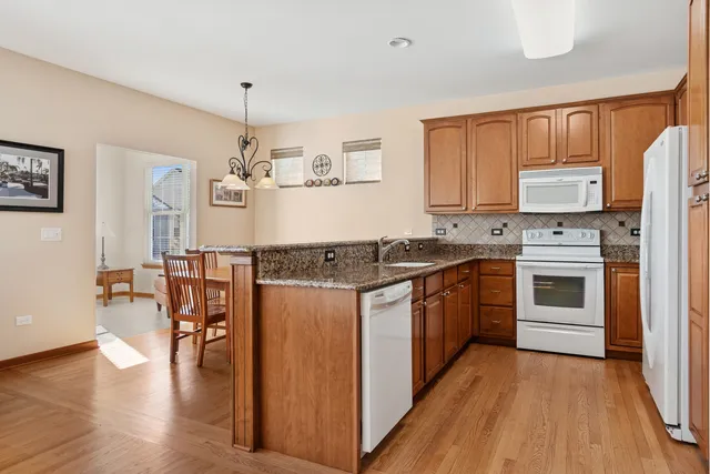 a kitchen with stainless steel appliances granite countertop a stove top oven a sink dishwasher and a refrigerator with wooden floor