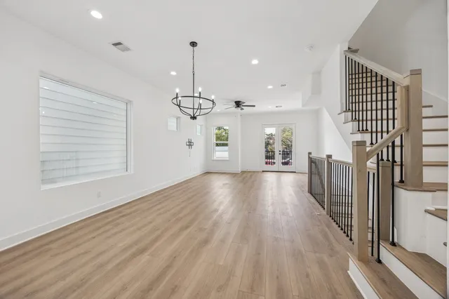 an empty room with wooden floor staircase and windows