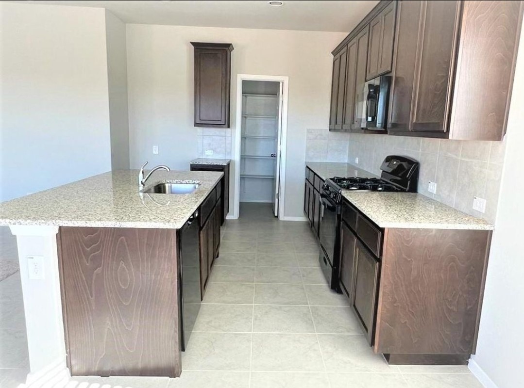 2771 Winding Creek Road Kyle, TX 78640 - Photo 6 of 24 Granite counters and dark wood cabinetry provide a sophisticated look in this modern kitchen.
