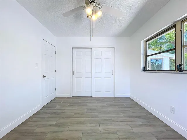 an empty room with wooden floor chandelier fan and windows