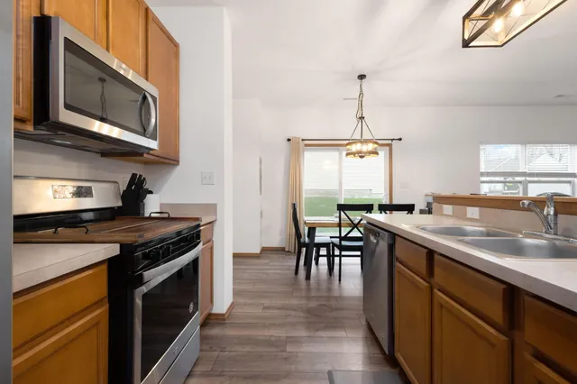 a kitchen with stainless steel appliances granite countertop a stove top oven a sink dishwasher a dining table and chairs with wooden floor