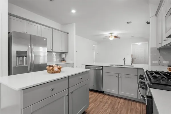 a kitchen with a sink dishwasher a stove and white cabinets with wooden floor