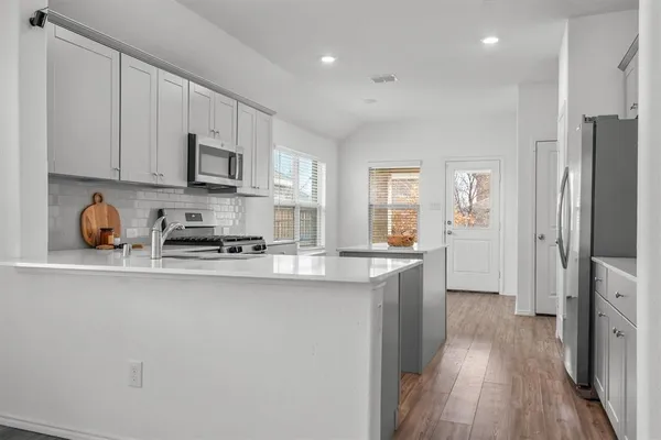 a kitchen with stainless steel appliances granite countertop a refrigerator a sink dishwasher a stove and white countertops with wooden floor