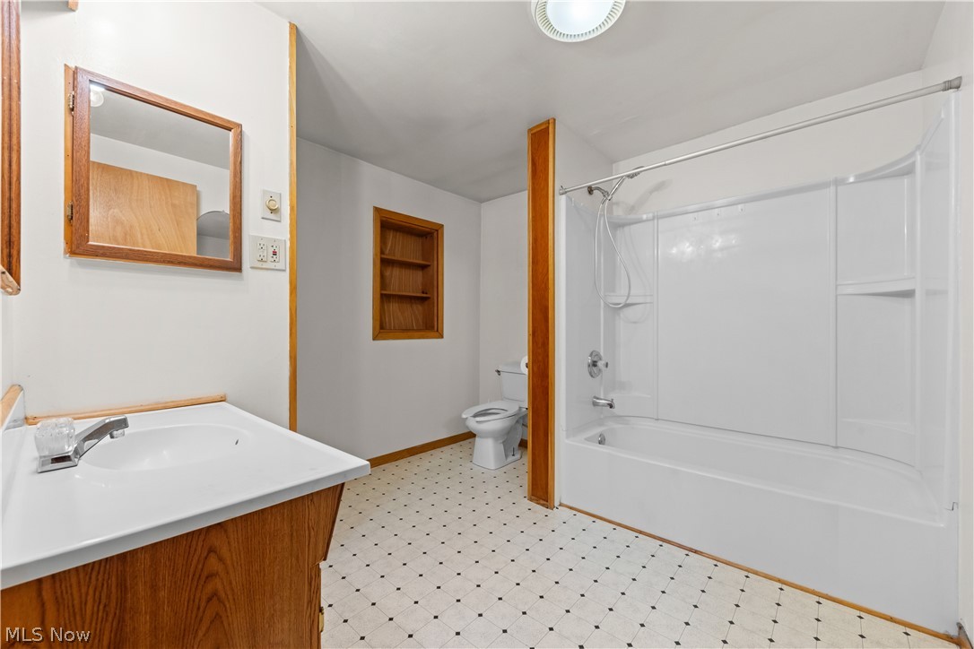 409 Edith Avenue Akron, OH 44312 - Photo 17 of 45 Bathroom featuring a white vanity with integrated sink, a wood-framed medicine cabinet, a built-in shower/tub combination with integrated shelving, patterned floor tiles, and a recessed wall shelf with wood trim