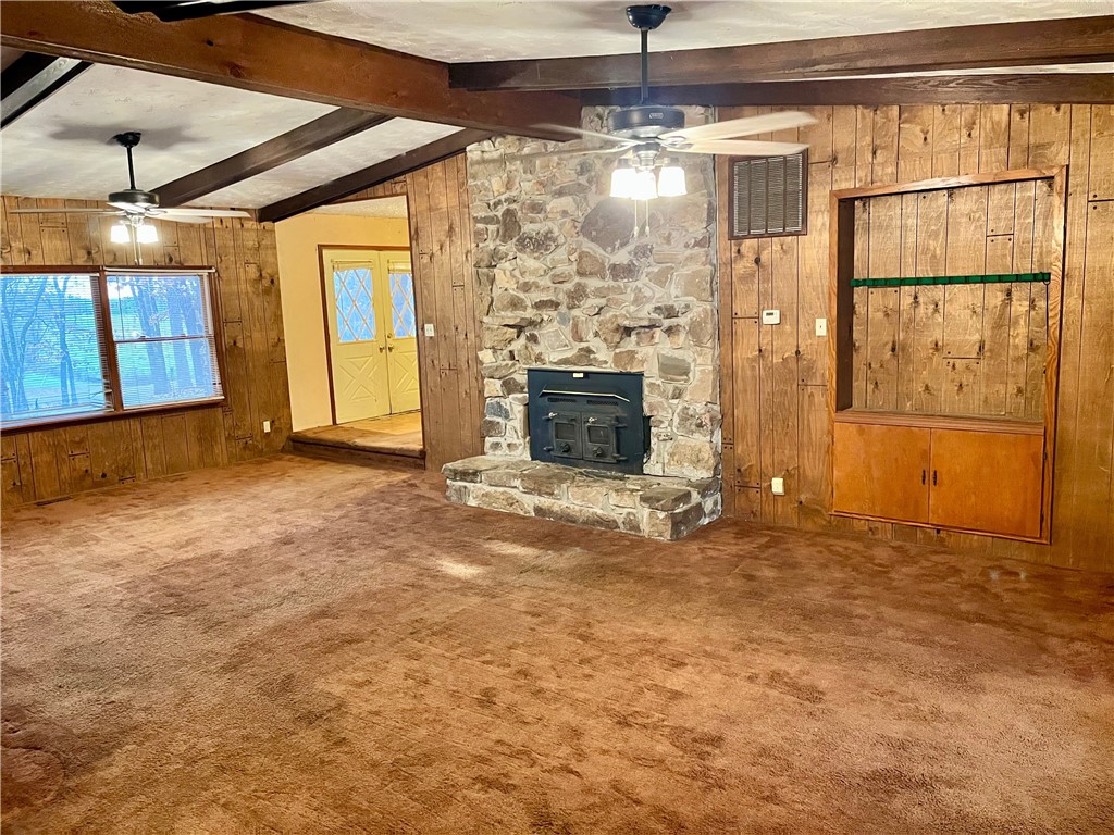 840 Miller Road Ola, AR 72853 - Photo 7 of 23 Unfurnished living room featuring wooden walls, a wood stove, a ceiling fan, and carpet