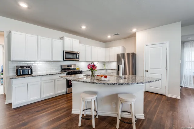 a kitchen with stainless steel appliances granite countertop a stove a sink a microwave a refrigerator and white cabinets with wooden floor