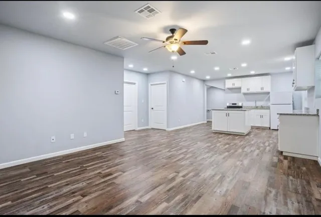 a view of an empty room and kitchen with wooden floor