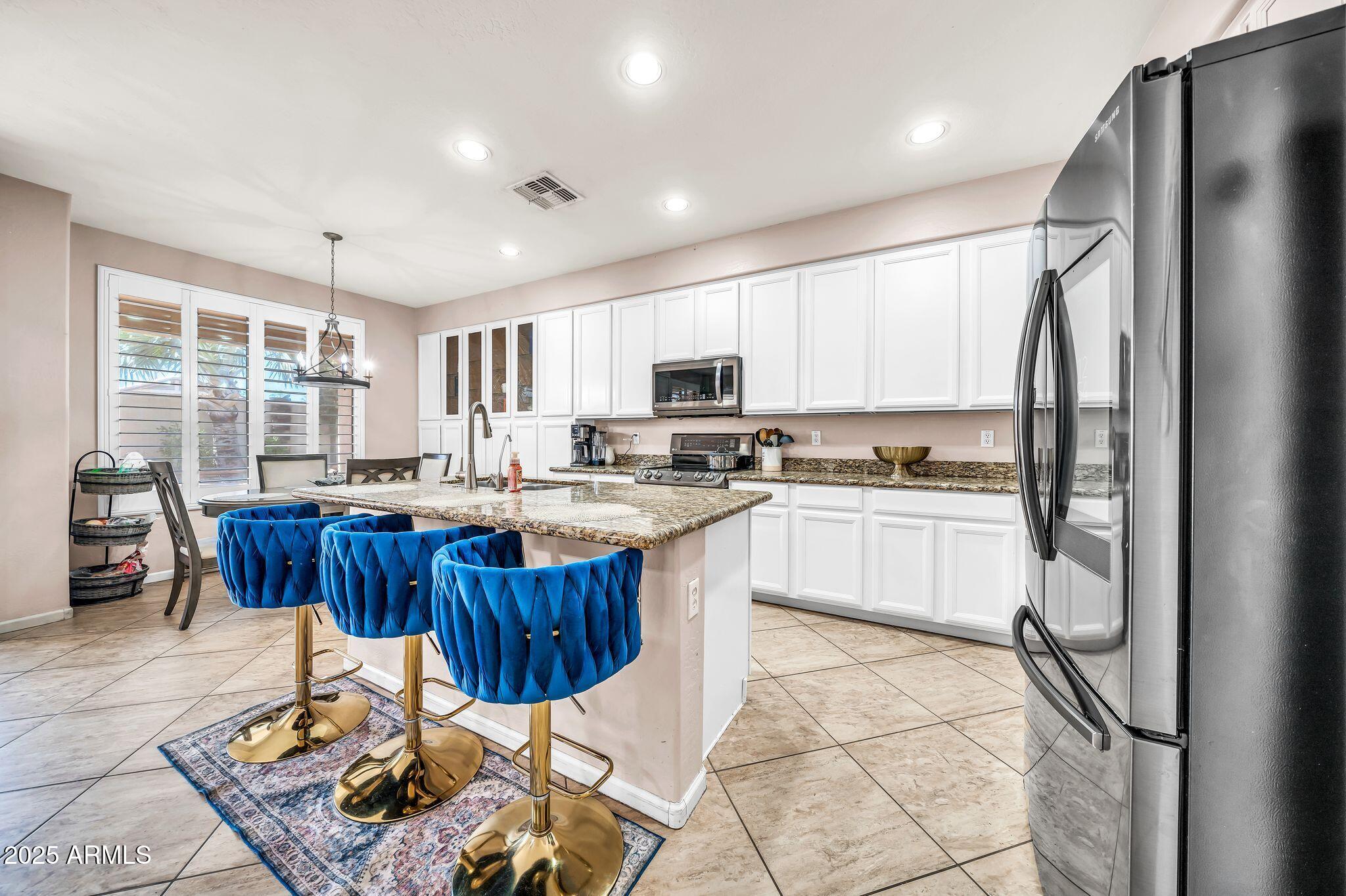 2292 South 155th Lane Goodyear, AZ 85338 - Photo 13 of 62 a kitchen with stainless steel appliances granite countertop a stove a sink dishwasher a refrigerator and a dining table with wooden cabinet