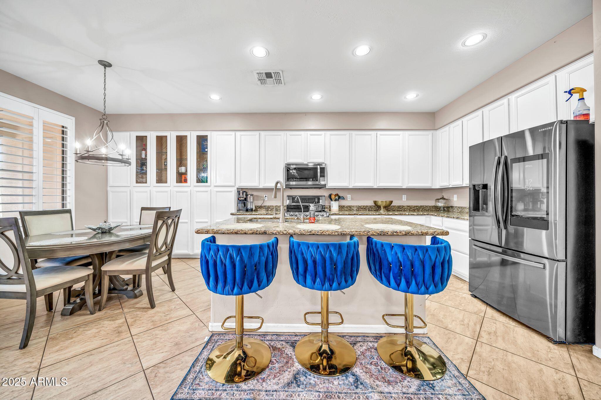 2292 South 155th Lane Goodyear, AZ 85338 - Photo 18 of 62 a kitchen with stainless steel appliances granite countertop a refrigerator a stove a sink dishwasher a dining table and chairs with wooden floor