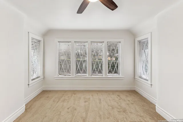 an empty room with chandelier fan and windows