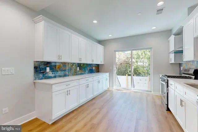 a kitchen with stainless steel appliances granite countertop a stove a sink and white cabinets with wooden floor