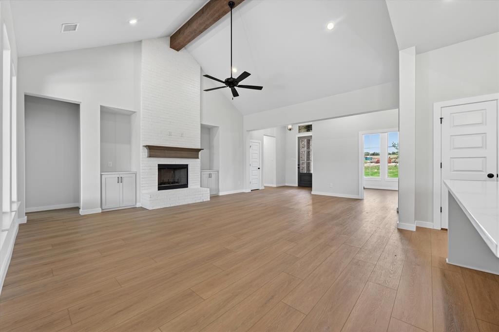 409 Mcalpine Springtown, TX 76082 - Photo 9 of 38 Vaulted ceiling with exposed wood beam, white brick fireplace with wood mantel, built-in cabinetry, wood-finish flooring, and recessed lighting