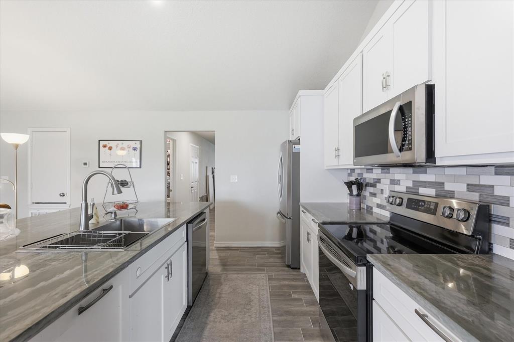 110 Highview Road Ennis, TX 75119 - Photo 13 of 40 Kitchen featuring white cabinetry, stainless steel appliances, a tile backsplash with varied grey and white tones, and wood-finish flooring