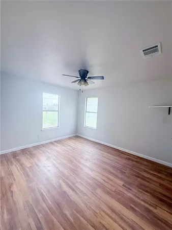 an empty room with wooden floor chandelier fan and windows