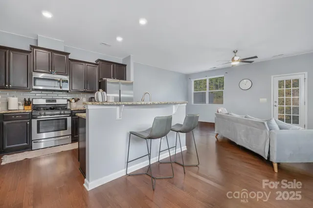 a kitchen with stainless steel appliances granite countertop a stove top oven a sink dishwasher a dining table and chairs with wooden floor