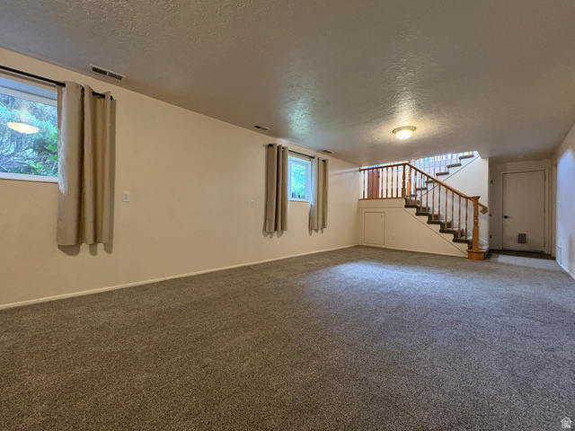 595 Meadowlark Road Orem, UT 84097 - Photo 53 of 87 Spacious carpeted room featuring a wooden staircase with balusters, two windows with textile curtains, recessed under-stair storage, and overhead lighting
