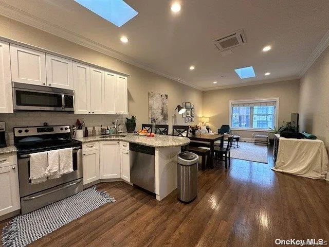 a open kitchen with stainless steel appliances granite countertop a stove top oven a sink dishwasher a dining table and chairs with wooden floor