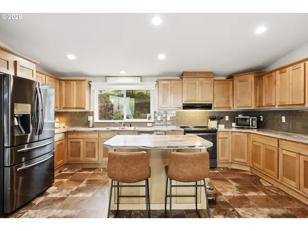 a kitchen with stainless steel appliances kitchen island granite countertop a refrigerator a stove a sink a dining table and chairs