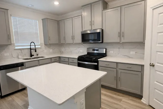 a kitchen with stainless steel appliances a sink dishwasher a stove top oven a refrigerator with white cabinets and wooden floor