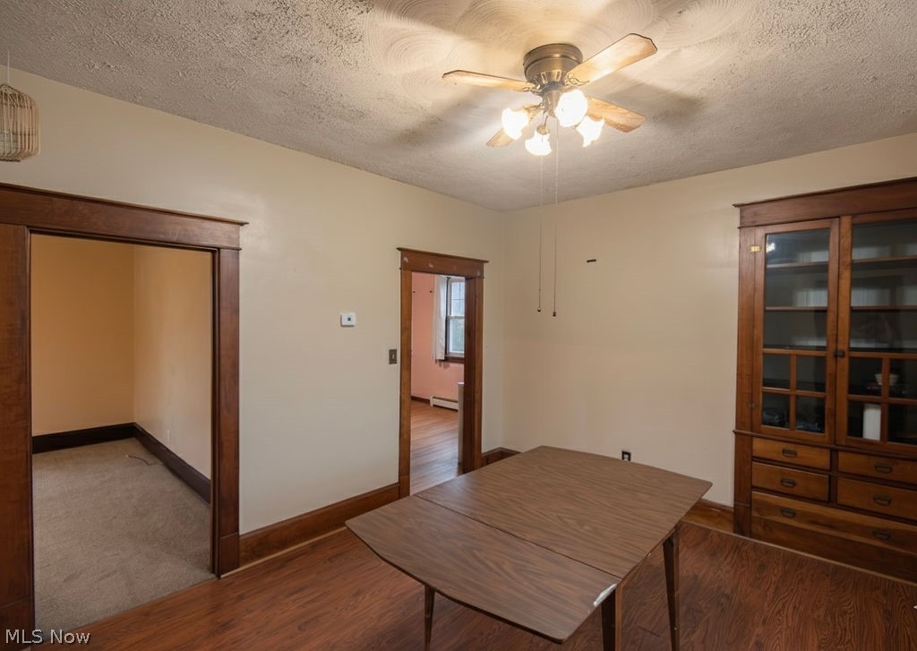 1195 South Johnson Road Sebring, OH 44672 - Photo 8 of 34 Unfurnished dining area with a textured ceiling, a ceiling fan, dark wood-style flooring, and baseboard heating