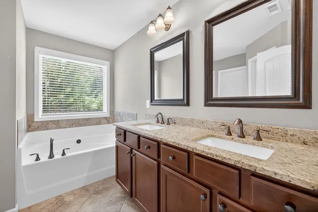 a bathroom with double vanity sinks a large mirror and a bathtub