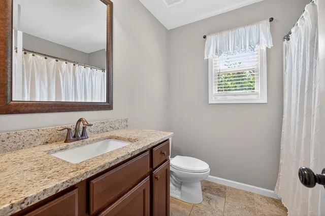a bathroom with a granite countertop sink toilet and a window