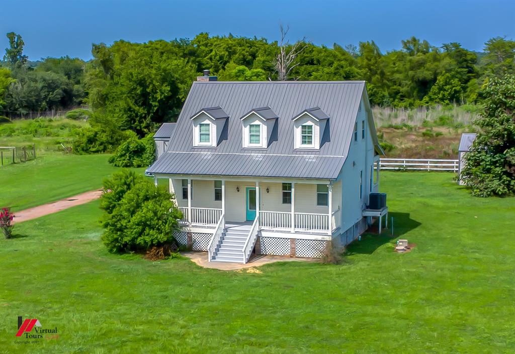Gable-front home featuring a gray metal roof, three dormer windows, and a covered front porch with white railings