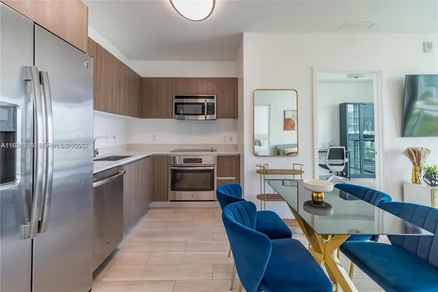 a kitchen with stainless steel appliances granite countertop a refrigerator a stove top oven a sink dishwasher and couches with wooden floor