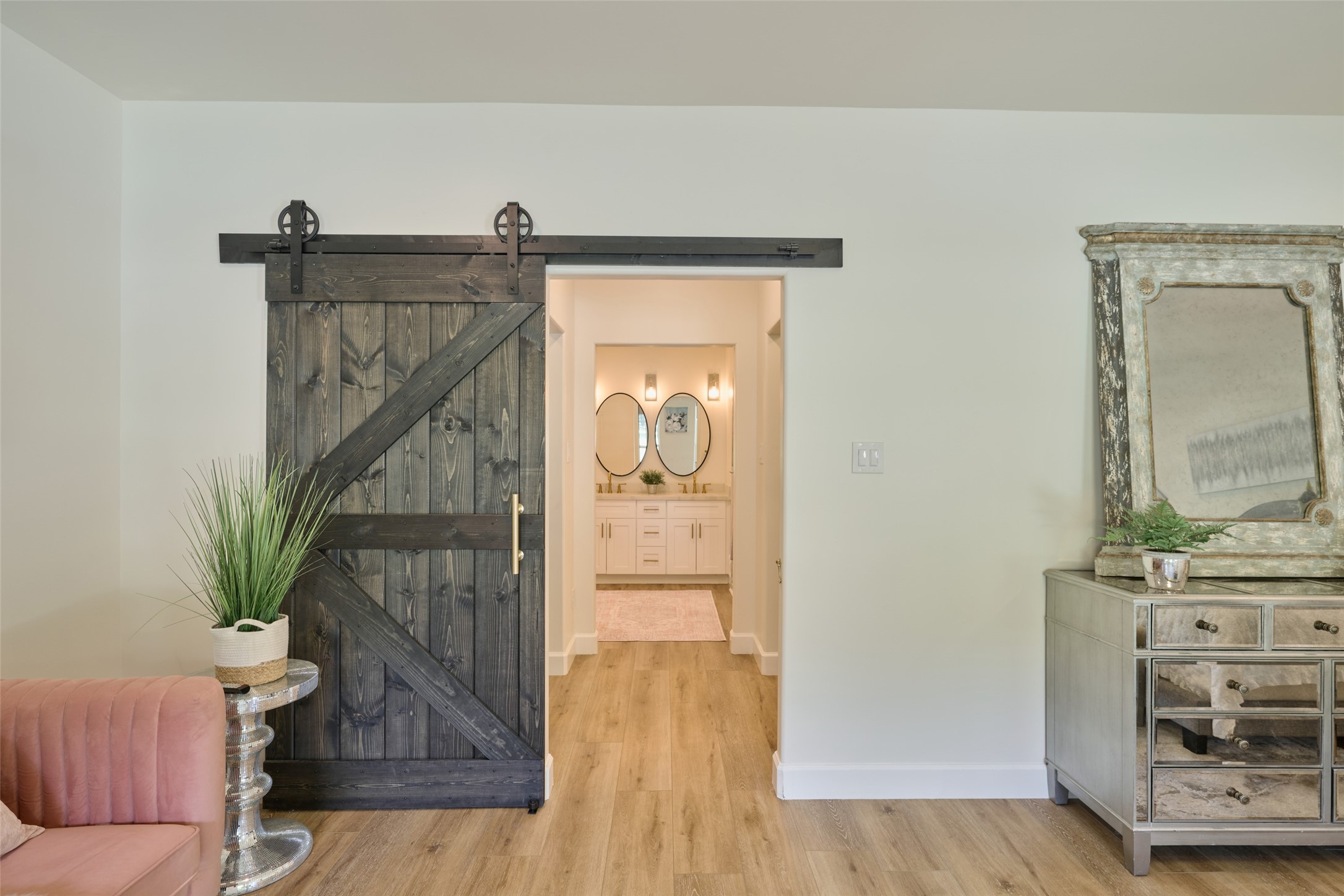 2218 Honea Egypt Road Magnolia, TX 77354 - Photo 30 of 50 This photo features an elegant interior with a rustic sliding barn door, light hardwood floors, and a chic mirrored console table, complemented by a cozy pink chair and decorative plants, creating a warm and welcoming space.