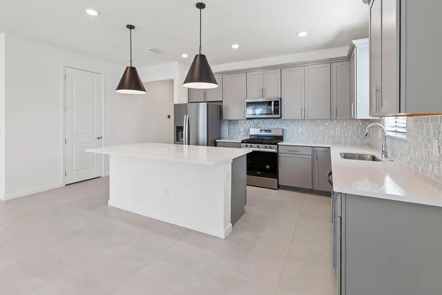 a kitchen with stainless steel appliances granite countertop a sink a stove a refrigerator and white cabinets