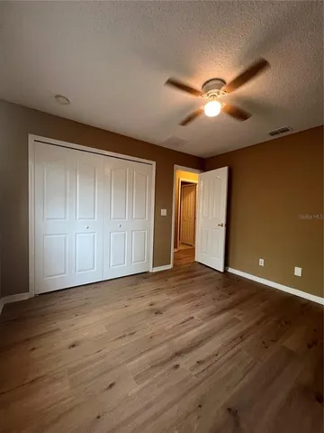 a view of an empty room with wooden floor and a ceiling fan