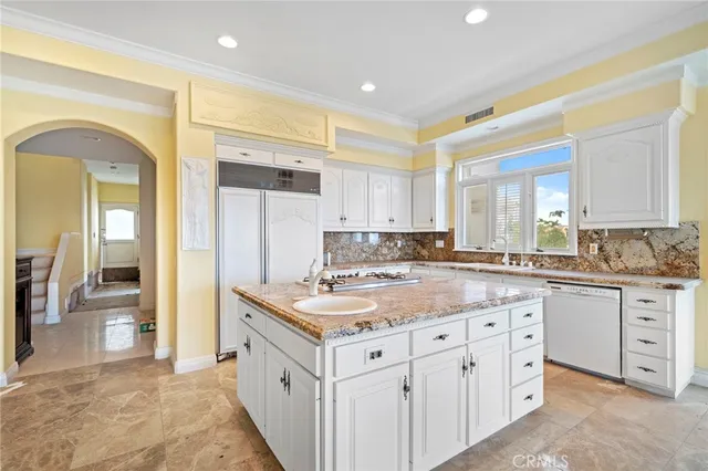 a kitchen with kitchen island granite countertop a stove a sink a refrigerator and white cabinets with wooden floor