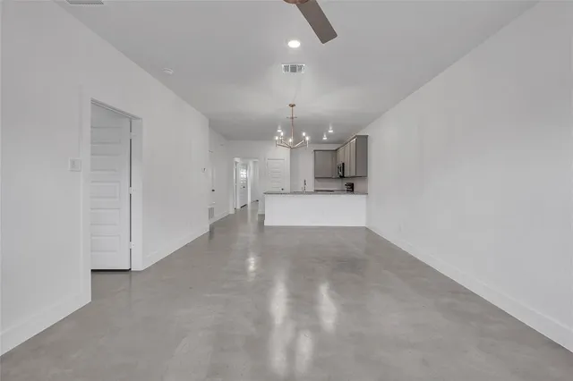 an empty room with kitchen and chandelier fan
